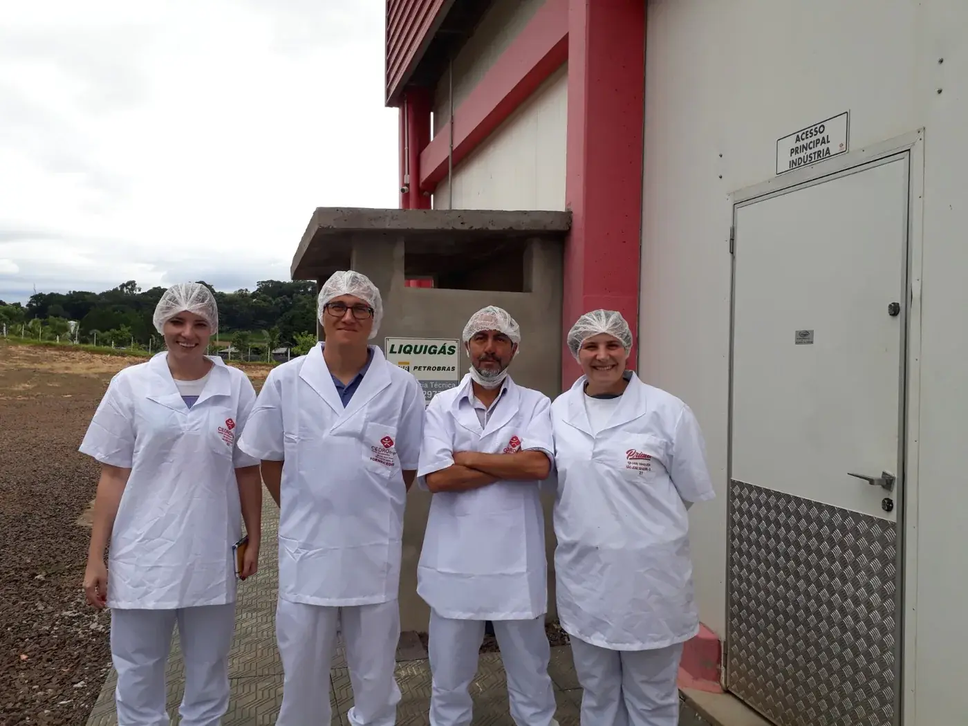 Equipe técnica da EGN de avental e touca no acesso principal de uma unidade frigorífica no Oeste de Santa Catarina, durante auditoria ambiental